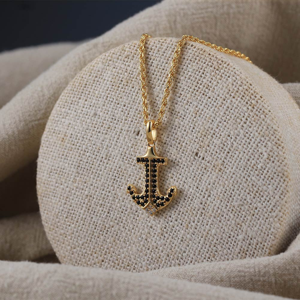Gold necklace with an anchor pendant on a textured beige surface