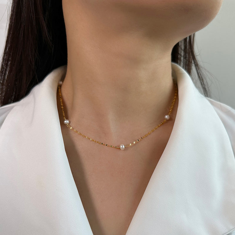 Gold necklace with pearls worn by a person against a neutral background