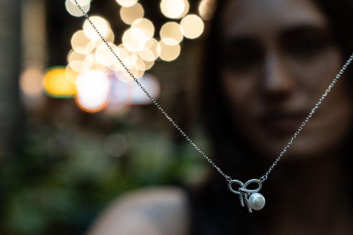 Necklace with a heart-shaped pendant worn by a person against a blurred background with lights.