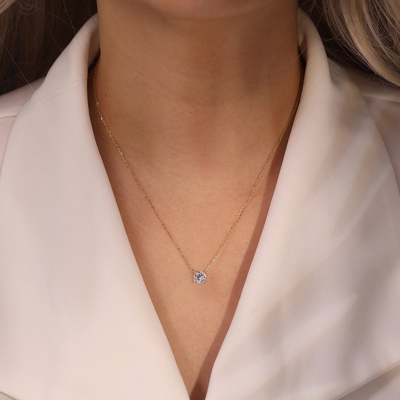 Gold necklace with a diamond pendant worn by a person in a light-colored shirt.
