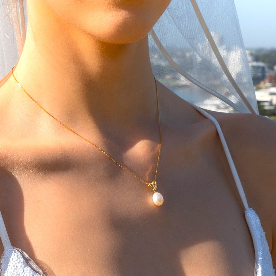 Close-up of a necklace with a pearl pendant on a blurred outdoor background