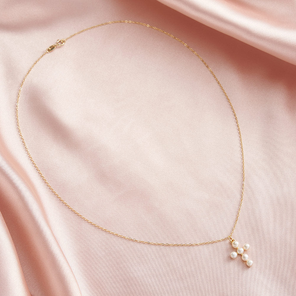 Gold necklace with a pearl cross on a pick fabric background