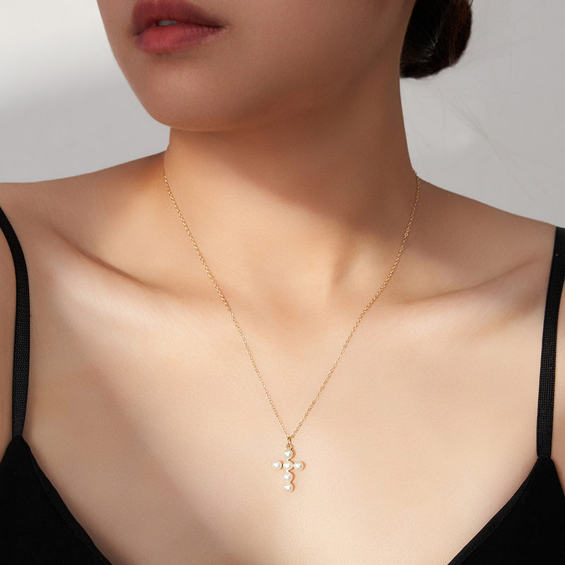 Gold necklace with a cross pendant on a model against a neutral background
