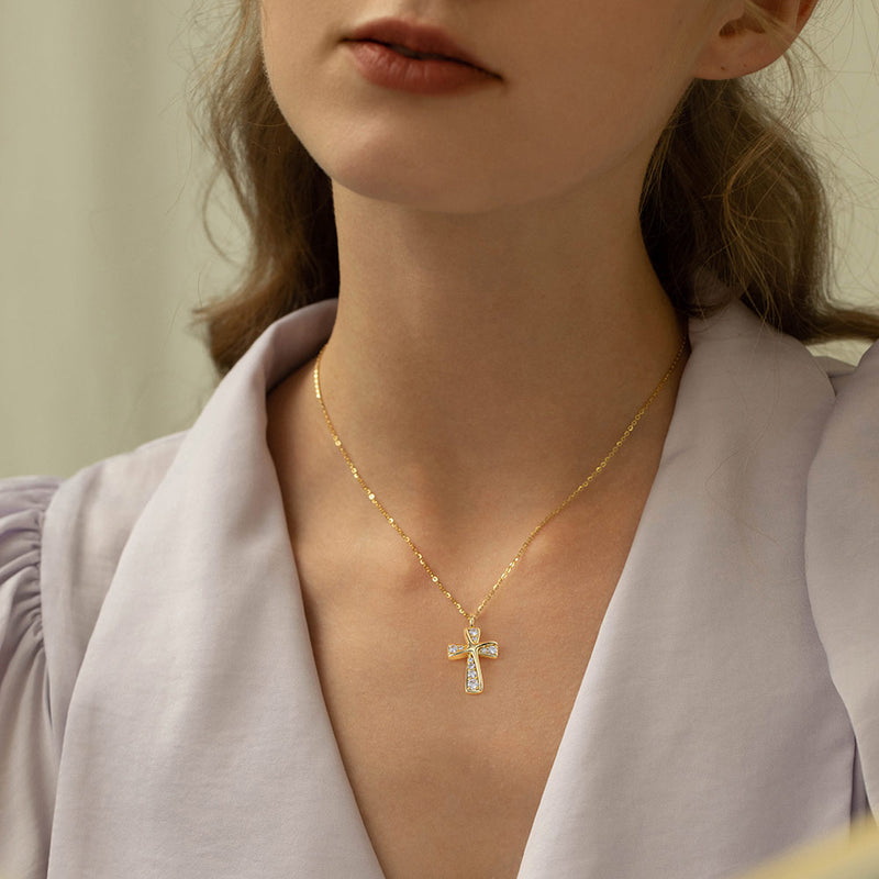 Close-up of a person wearing a gold necklace with a cross pendant.