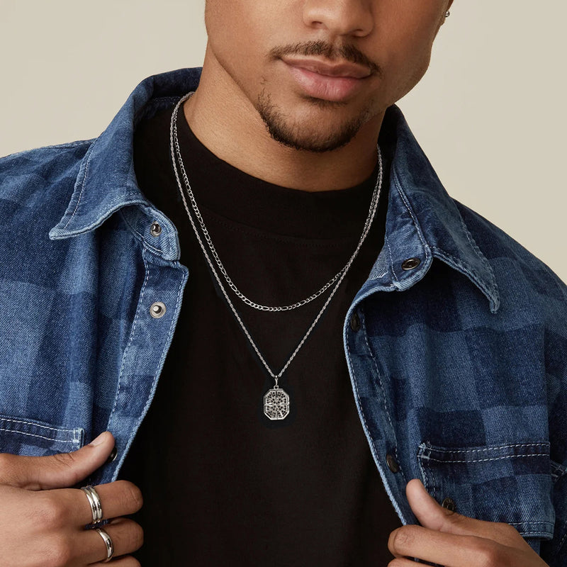 Man wearing a denim jacket over a black shirt with a silver necklace featuring a pendant.