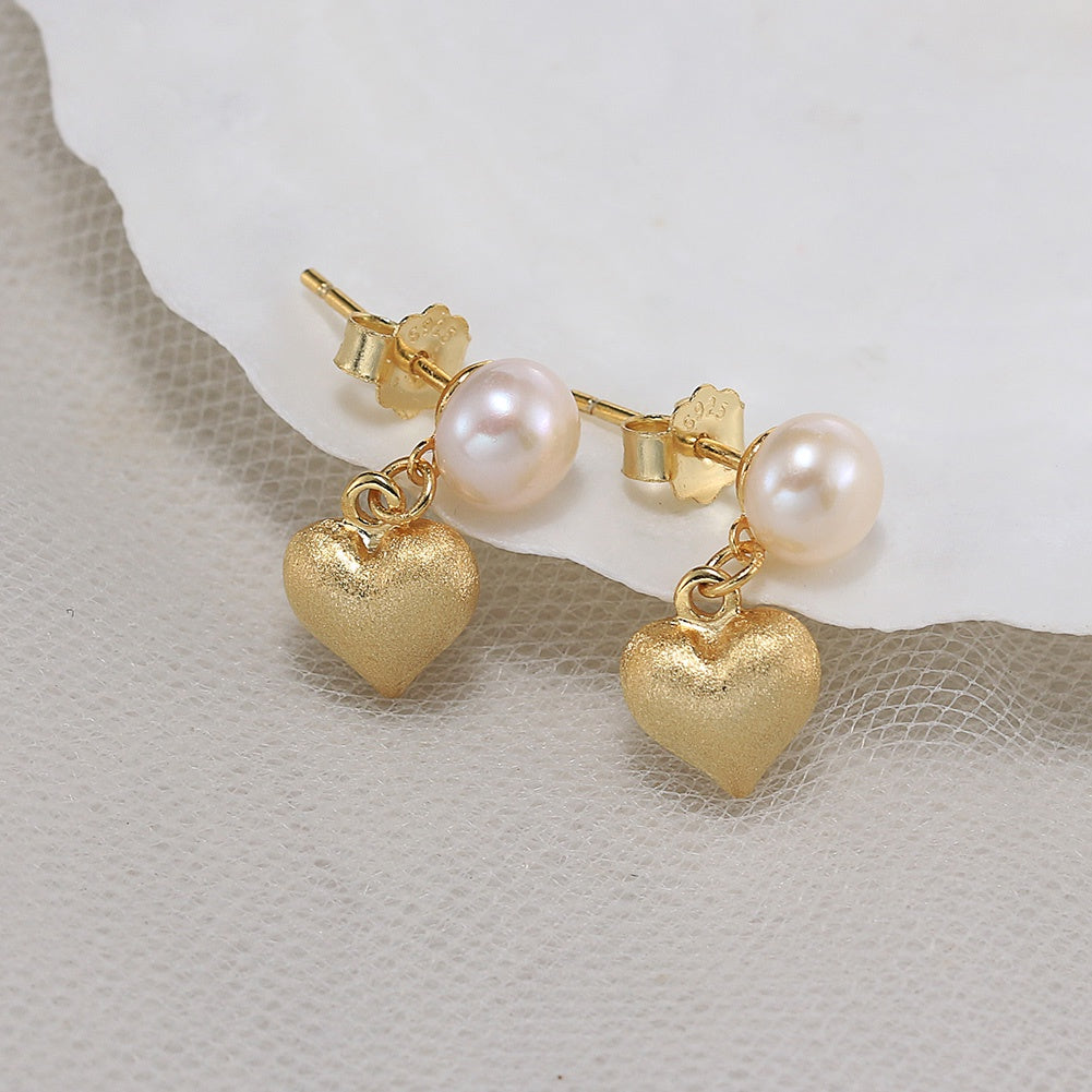 Gold heart-shaped earrings with pink pearls on a textured surface