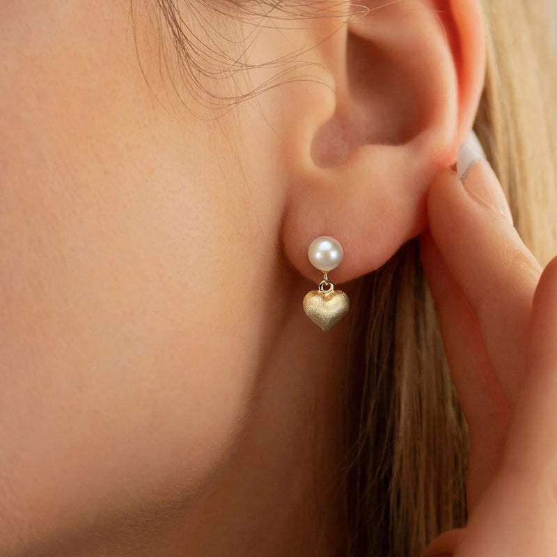 Close-up of a person wearing pearl and gold heart-shaped earrings.