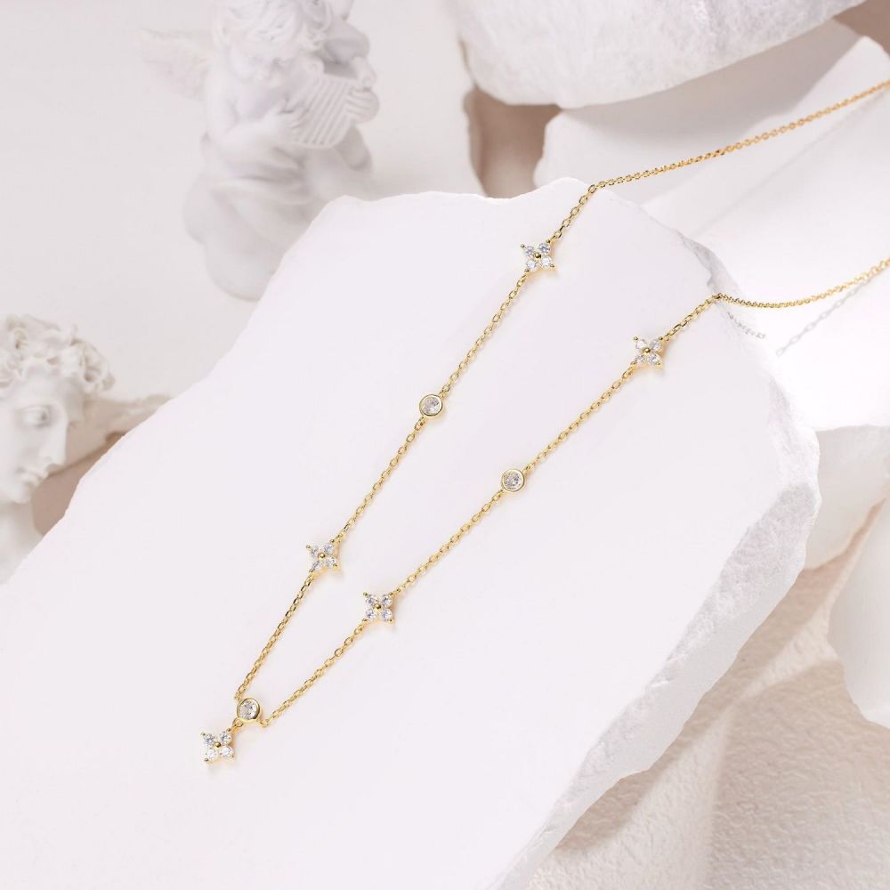 Troika necklace layed out on the white background featuring gold pendants with cubic zirconias