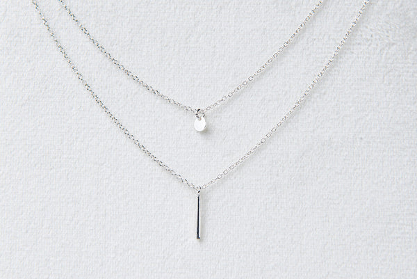 A silver necklace with a double layer of chains and a fixed pendant featuring a small bead.