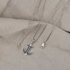 Silver anchor necklace with black stones on a beige fabric background