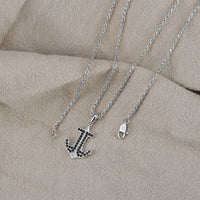 Silver anchor necklace with black stones on a beige fabric background