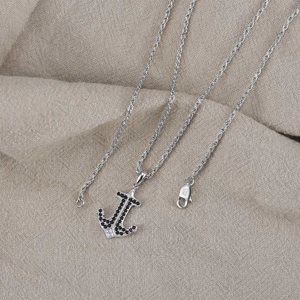 Silver anchor necklace with black stones on a beige fabric background