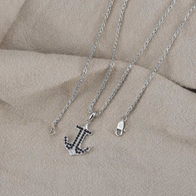 Silver anchor necklace with black stones on a beige fabric background