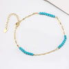 A gold-colored anklet with turquoise beads and an extension chain.