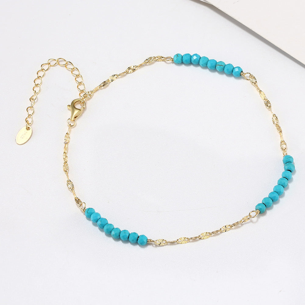 A gold-colored anklet with turquoise beads and an extension chain.
