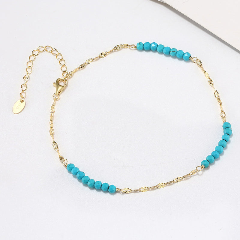 A gold-colored anklet with turquoise beads and an extension chain.