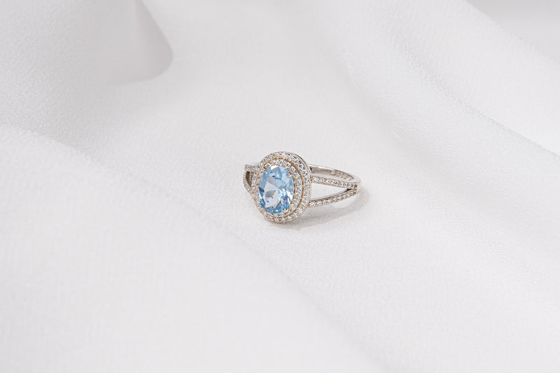 Silver ring featuring a light blue gem stone and cubic zirconias on a white background