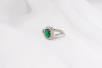 Silver ring featuring a vivid green gem stone and cubic zirconias on a white background