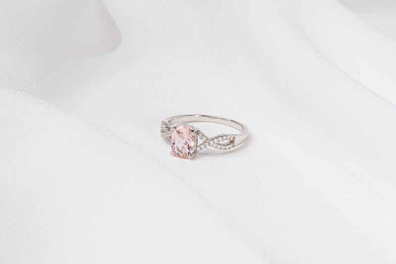 Silver ring featuring a light pink gem stone and cubic zirconias on a white background