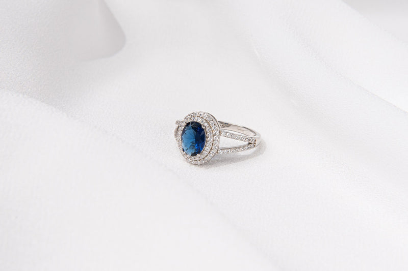 Silver ring featuring a deep blue gem stone and cubic zirconias on a white background