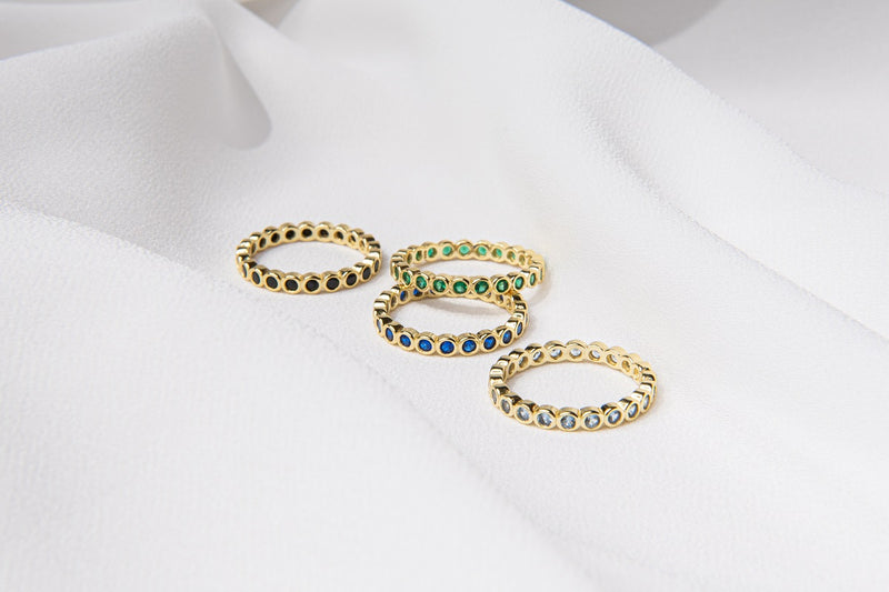 A set of four gold vermeil rings with colorful stone accents placed on a white fabric surface.