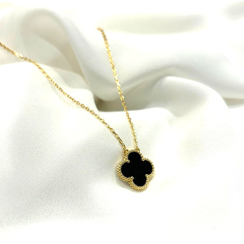 Gold necklace with a black clover pendant on a white fabric background