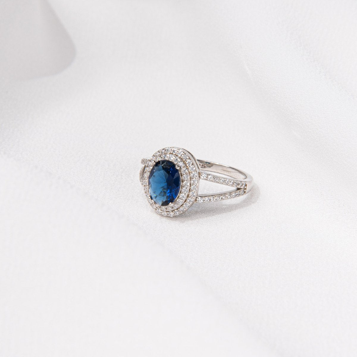 Silver ring featuring a deep blue gem stone and cubic zirconias on a white background