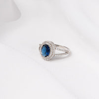 Silver ring featuring a deep blue gem stone and cubic zirconias on a white background
