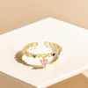 Gold open ring with heart-shaped gemstones on a beige surface