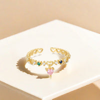 Gold open ring with heart-shaped gemstones on a beige surface