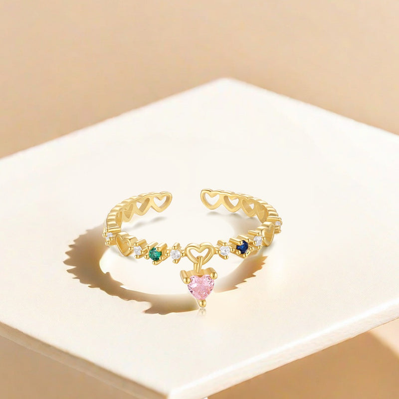 Gold open ring with heart-shaped gemstones on a beige surface