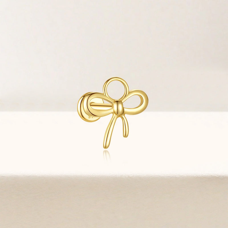 Gold bow-shaped earring on a light beige background