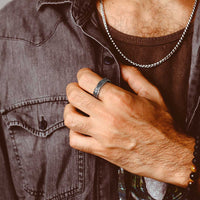 Man wearing a denim jacket and brown shirt with a focus on their silver ring 