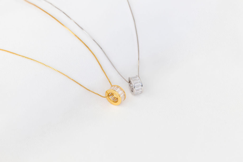 One silver and one gold fine chain necklaces eack with a pendant featuring cubic zirconias on a white background
