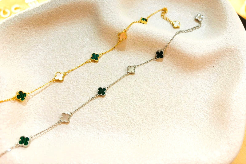 A gold and a silver bracelet with clover shaped charms on a fabric background