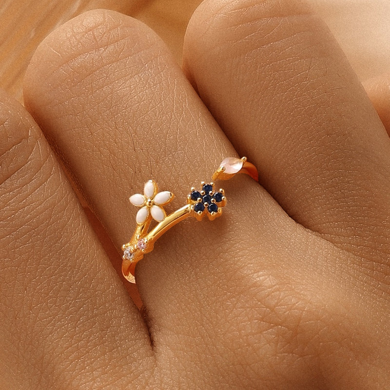 A gold vermeil ring with a cherry blossom design, featuring a thin band and adorned with small blue and white gemstones, displayed on a person's finger.