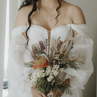 Woman in a white off-shoulder dress holding a bouquet of flowers wearing a classic pearl drop necklace