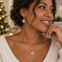 Model wearing the Snowfall snowflake earrings and pendant necklace set in gold, styled with a cozy knit by a lit Christmas tree