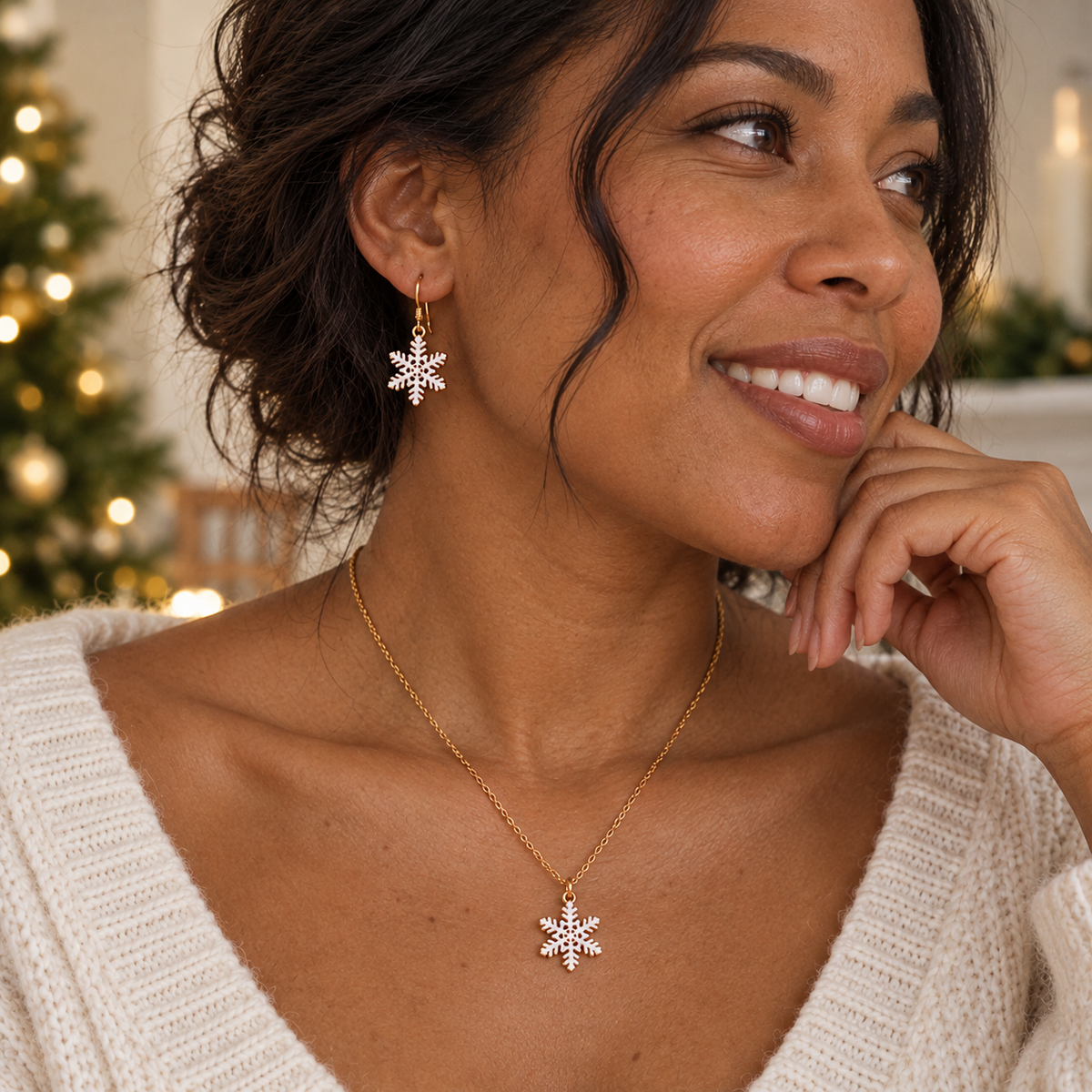 Model wearing the Snowfall snowflake earrings and pendant necklace set in gold, styled with a cozy knit by a lit Christmas tree