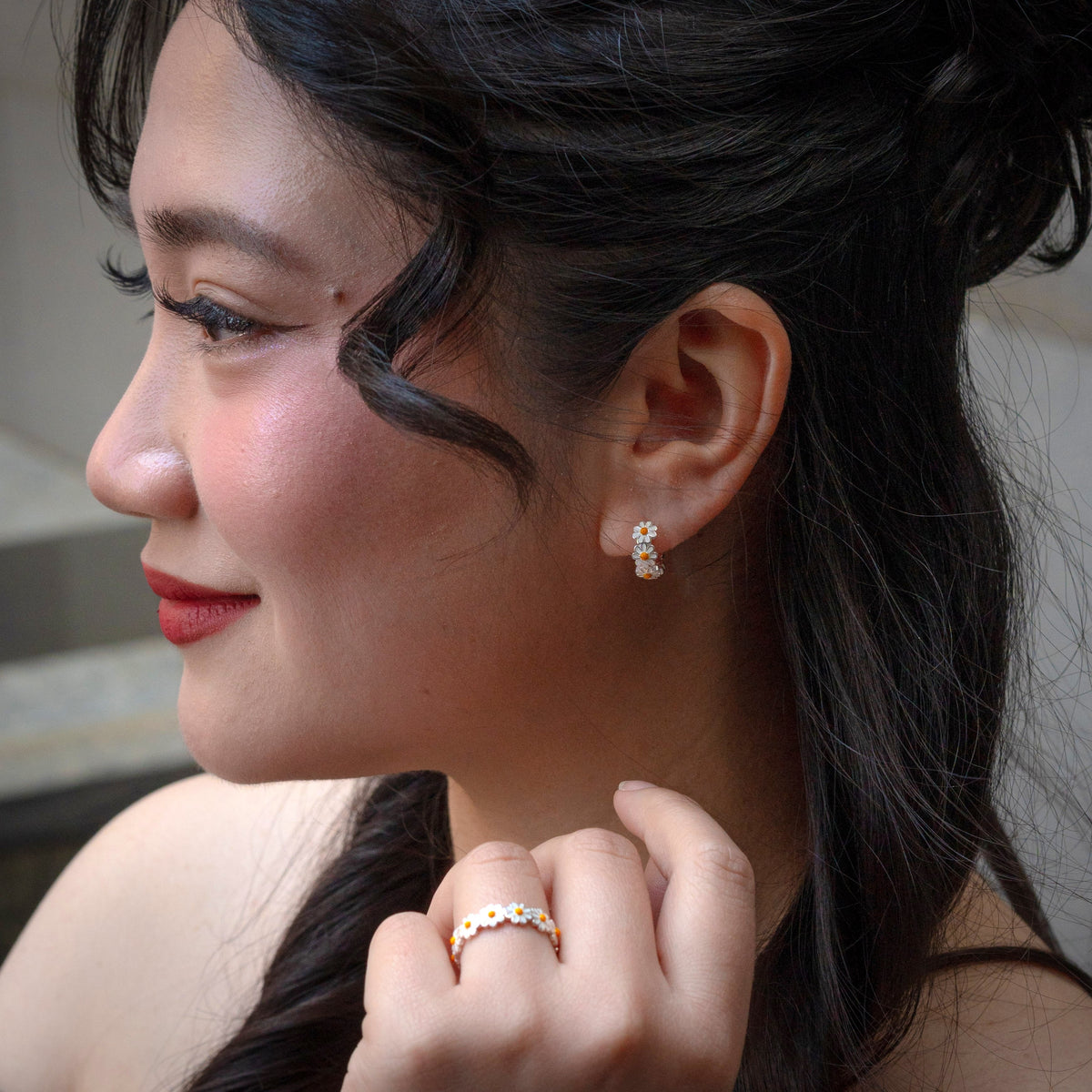 Close-up of a woman wearing daisy flower earrings & ring 