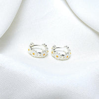 A pair of sterling silver hoop earrings with daisy-shaped embellishments, displayed on a white fabric surface.
