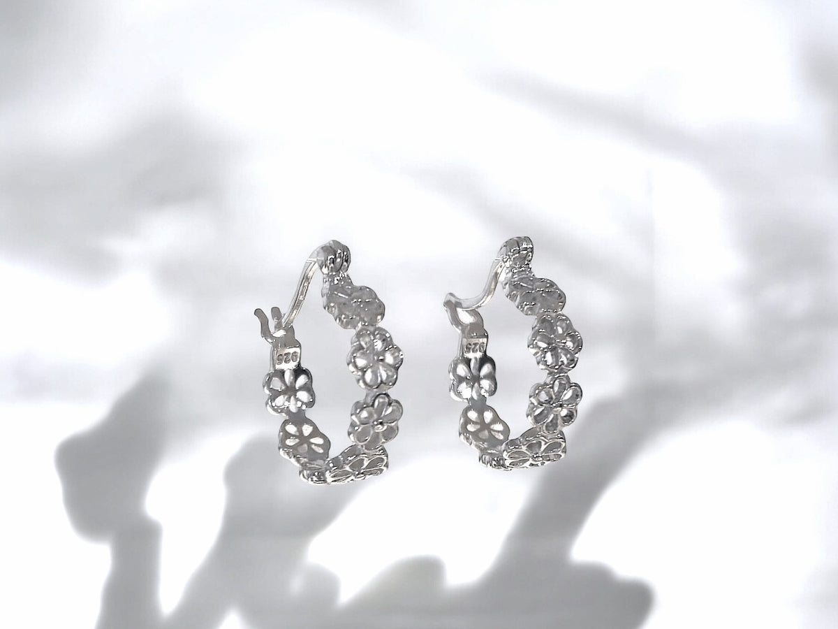 This image features a pair of elegant huggie earrings, named "Daisy and Me Huggies." The earrings are crafted in a sparkling silver material and are designed with a delicate floral pattern that wraps around the ear.