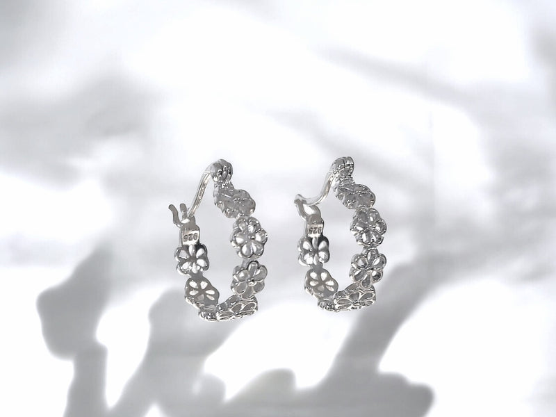 This image features a pair of elegant huggie earrings, named "Daisy and Me Huggies." The earrings are crafted in a sparkling silver material and are designed with a delicate floral pattern that wraps around the ear.