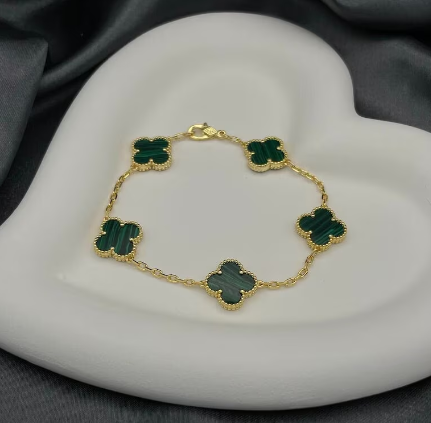 A gold-colored bracelet with green clover-shaped charms, displayed on a white plate.
