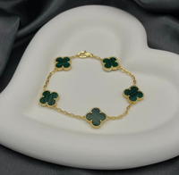 A gold-colored bracelet with green clover-shaped charms, displayed on a white plate.