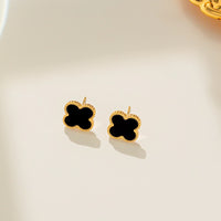 This image displays a pair of elegant Daphne earrings, featuring a simple yet sophisticated design. The earrings are crafted in the shape of clovers, each composed of a single, smooth black stone set within a meticulously crafted gold frame.