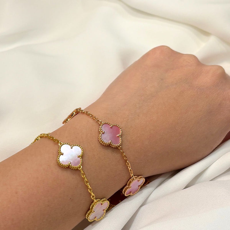 Gold bracelet with pink clover-shaped charms on a wrist against a white background
