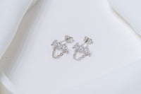A pair of silver stud earrings with dangle loops and butterfly backs, placed on a white fabric surface.