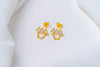 A pair of gold-colored stud earrings with dangle loops and butterfly backs, placed on a white fabric surface.