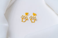 A pair of gold-colored stud earrings with dangle loops and butterfly backs, placed on a white fabric surface.